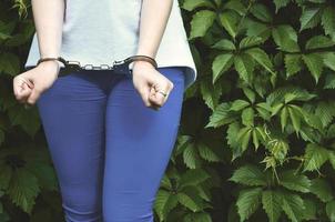 fragmento do corpo de uma jovem criminosa com as mãos algemadas contra um fundo de folhas de hera verde florescente. o conceito de detenção de um criminoso de uma criminosa feminina em um ambiente rural foto