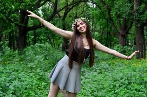 retrato de uma jovem emocional com uma coroa de flores na cabeça e enfeites brilhantes na testa. linda morena posando em uma bela floresta florescente durante o dia em um belo dia foto