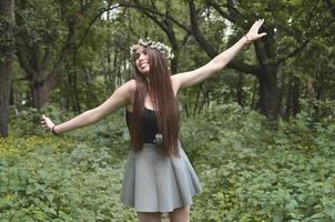 uma foto da floresta de uma bela jovem morena de aparência européia com olhos castanhos escuros e lábios grandes. na cabeça da menina está uma coroa de flores, na testa enfeites brilhantes