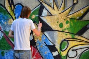 foto no processo de desenho de um padrão de graffiti em uma velha parede de concreto. jovem loiro de cabelos compridos desenha um desenho abstrato de cores diferentes. arte de rua e conceito de vandalismo