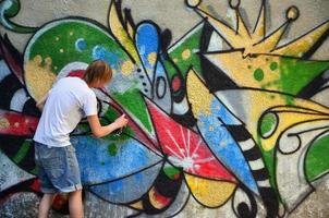 foto no processo de desenho de um padrão de graffiti em uma velha parede de concreto. jovem loiro de cabelos compridos desenha um desenho abstrato de cores diferentes. arte de rua e conceito de vandalismo