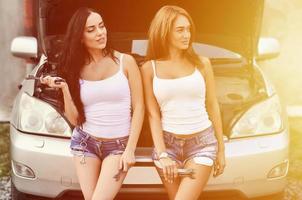 duas garotas jovens e sensuais com chaves de roda em torno de um ca prateado foto