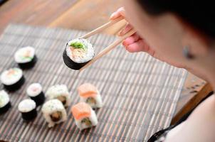 menina morena com pauzinhos detém um rolo de sushi em um fundo de esteira de serwing palha de bambu. comida tradicional asiática foto