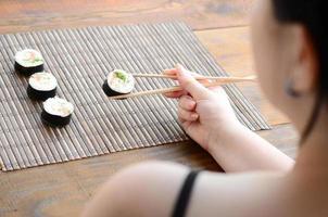 menina morena com pauzinhos detém um rolo de sushi em um fundo de esteira de serwing palha de bambu. comida tradicional asiática foto