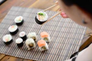 menina morena com pauzinhos detém um rolo de sushi em um fundo de esteira de serwing palha de bambu. comida tradicional asiática foto