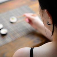 menina morena com pauzinhos detém um rolo de sushi em um fundo de esteira de serwing palha de bambu. comida tradicional asiática foto