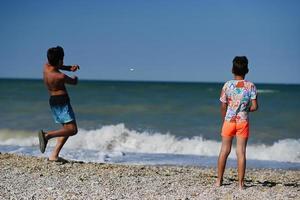 dois irmãos jogam pedras no mar na praia porto sant elpidio, itália. foto