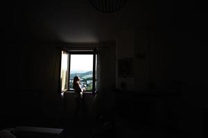 garota de pé e olhando da janela no pôr do sol. foto