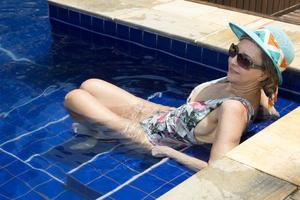 mulher relaxando na piscina usando um chapéu azul e óculos escuros foto