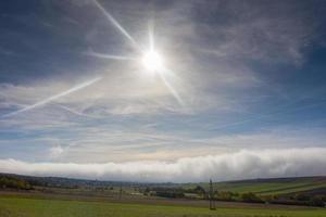 sol brilhando no céu azul sobre uma parede branca de denso nevoeiro foto