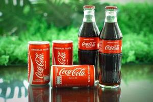 ayutthaya, tailândia-25 de junho de 2020- clássico da coca-cola em uma garrafa de vidro e lata em fundo de cimento em tons escuros. coca cola, o coque é o refrigerante carbonatado mais popular vendido em todo o mundo foto