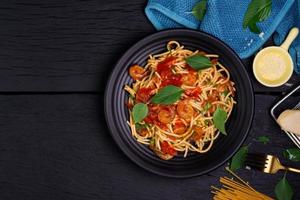 delicioso macarrão espaguete com camarão e queijo servido em um prato preto sobre uma receita italiana de mesa de fundo preto, molho de tomate, legumes e especiarias vista superior com espaço de cópia