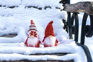 cartão de férias de natal gnomos escandinavos fofos com chapéu vermelho e barba branca no banco de inverno nevado conto de fadas queda de neve inverno olá dezembro, janeiro, conceito de fevereiro feliz ano novo, natal foto