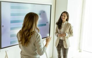 duas jovens discutindo resultados financeiros na tela grande da parede do escritório foto