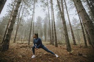 jovem com fato de treino azul alongamento antes do treino na floresta de outono foto