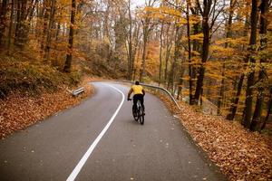 jovem andando de bicicleta em uma estrada rural através da floresta de outono foto