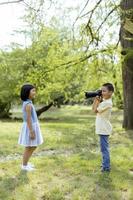 garotinho asiático agindo como um fotógrafo profissional enquanto tira fotos de sua irmãzinha