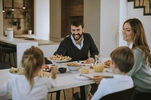 jovem família feliz conversando enquanto toma café da manhã na mesa de jantar foto