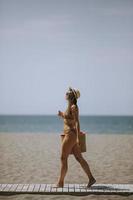 jovem mulher de biquíni com bolsa de palha na praia em dia de verão foto