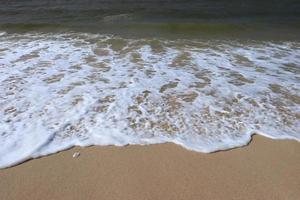 costa do oceano com praia de areia e onda avançando. espuma de água com areia lisa. belas ondas no fundo da praia de areia. foto