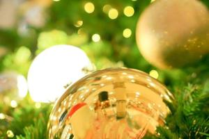 bolas de natal douradas decoradas em pinheiros no dia de natal com fundo de árvore de natal embaçado e bokeh de iluminação de natal. foto