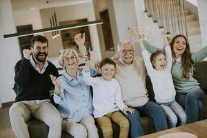 família de várias gerações assistindo futebol na tv e comemorando um gol, sentado no sofá da sala foto