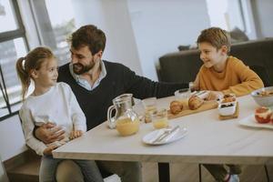 pai tomando café da manhã com seu filho e filha em casa foto