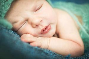 bebê recém-nascido dormindo docemente em um tapete azul com boné azul foto