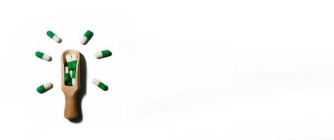 pílulas de medicina verde sobre fundo branco em uma colher de pau na forma de uma lâmpada. copie o espaço para o texto. bandeira foto