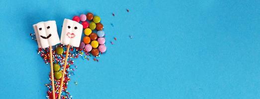 marshmallows em espetos de madeira com doces de cor sobre fundo azul. conceito de férias. doces em forma de pessoas. bandeira foto