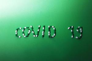 inscrição covid 19 de letras feitas de comprimidos em um fundo verde. conceito de vírus corona. foto