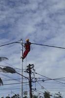 gorontalo-indonesia, dezembro de 2022 - técnicos conectam cabos a postes elétricos. empregado pendurado pelo cinto no poste de eletricidade para colocar o cabo de baixa tensão foto