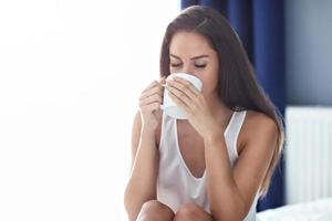 jovem mulher bonita sentada na cama com uma caneca de café foto