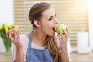 mulher adulta escolhendo entre maçã e rosquinha na cozinha foto