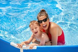 menino bonito com sua mãe brincando na piscina durante o verão foto