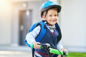 menino de escola em capacete de segurança andando de bicicleta com mochila foto