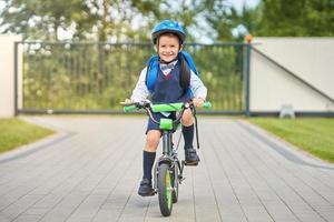 menino de escola em capacete de segurança andando de bicicleta com mochila foto