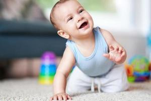 lindo menino sorridente rastejando no chão na sala de estar foto