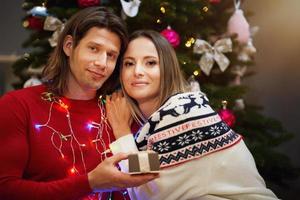 lindo casal adulto com presente sobre a árvore de natal foto