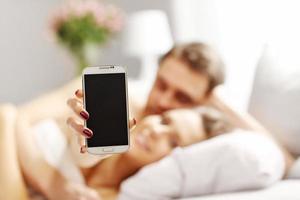 jovem casal na cama com smartphone foto