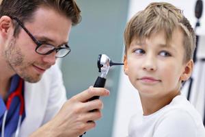 close-up do médico masculino examinando a orelha do menino com um otoscópio foto