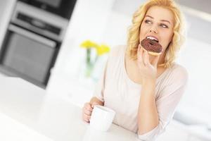 jovem mulher com donut e café na cozinha foto
