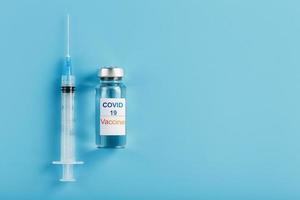 uma ampola com uma vacina e a inscrição covid-19 no rótulo da ampola, uma seringa para vírus e doenças em um fundo azul. foto