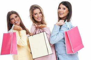 três mulheres em ternos pastel segurando sacolas de compras sobre fundo branco foto