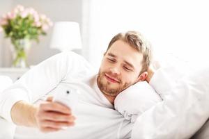 homem bonito, deitado na cama com smartphone foto