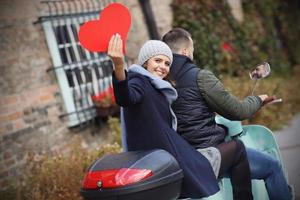 lindo casal jovem segurando corações enquanto andava de scooter na cidade no outono foto