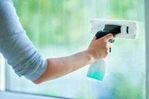 jovem mulher limpando janela na cozinha foto