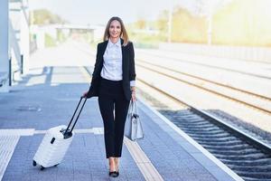 mulher elegante andando com bolsa e mala na estação ferroviária foto