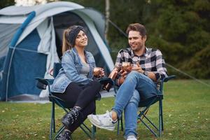 jovem casal simpático sentado em cadeiras na frente da barraca no acampamento foto