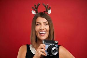 mulher adulta feliz em clima de natal tirando fotos instantâneas sobre fundo vermelho